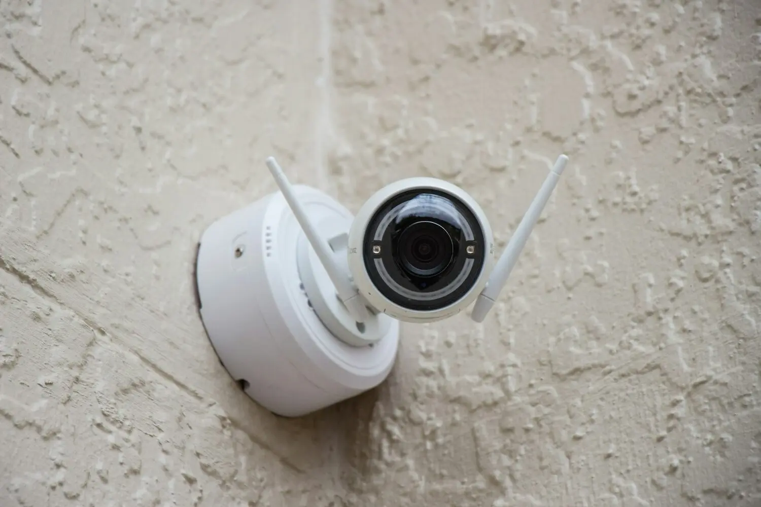 Cámara IP de seguridad blanca con antenas wifi instalada en la fachada de una vivienda