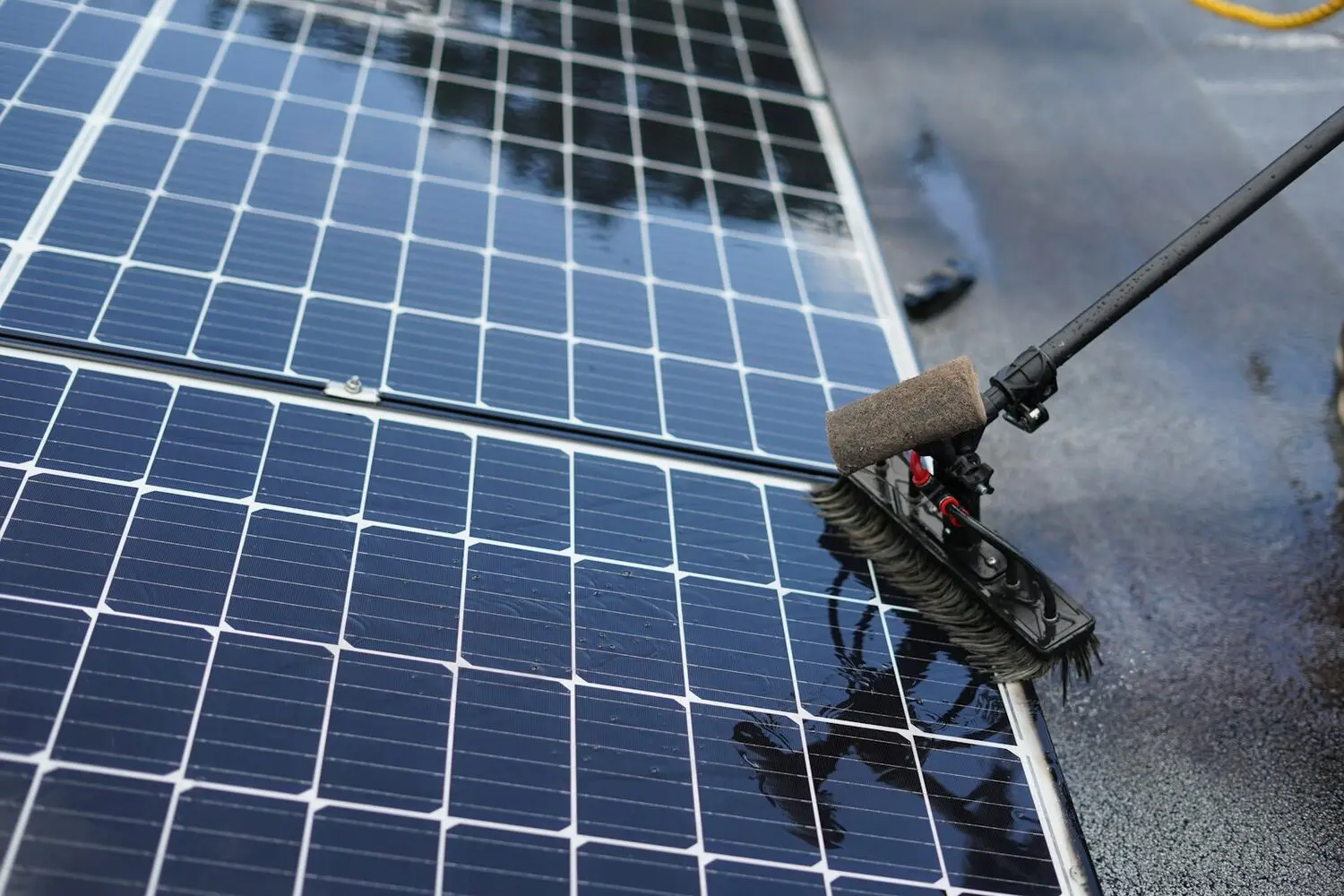 Limpieza de placas solares con cepillo de mango largo durante el mantenimiento