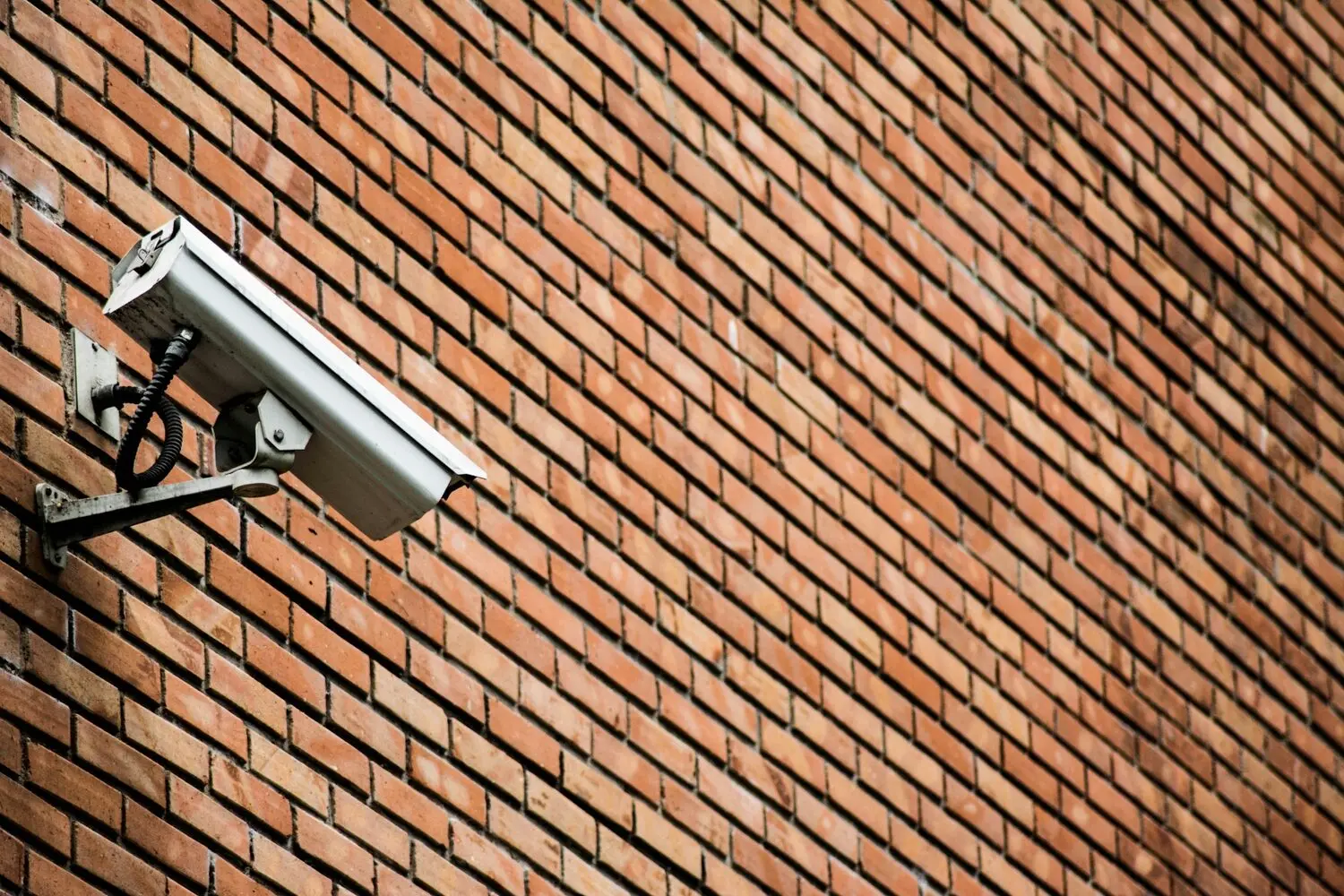 Cámara de seguridad exterior tipo bullet instalada sobre soporte metálico en un muro de ladrillo