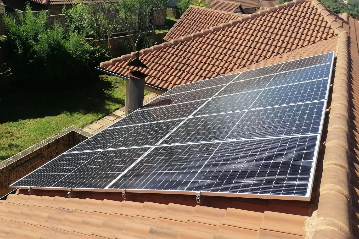 Placas solares sobre la cubierta de teja curva de una vivienda unifamiliar, vistas desde el tejado, con los módulos sujetos con raíles y grapas